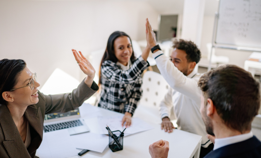 Erfolgreiche Zusammenarbeit im Team: Kolleginnen und Kollegen feiern eine gelungene Benefits-Strategie mit einem High Five im Büro.