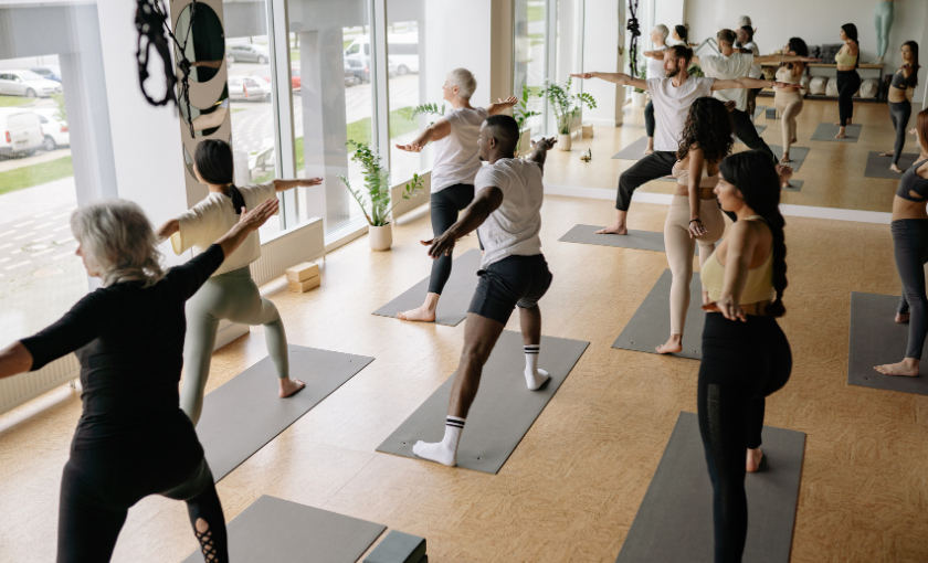 Eine Gruppe von Kollegen praktiziert gemeinsam Yoga in einem hellen Studio, als Beispiel für ein inklusives und gesundheitsförderndes Teamevent.