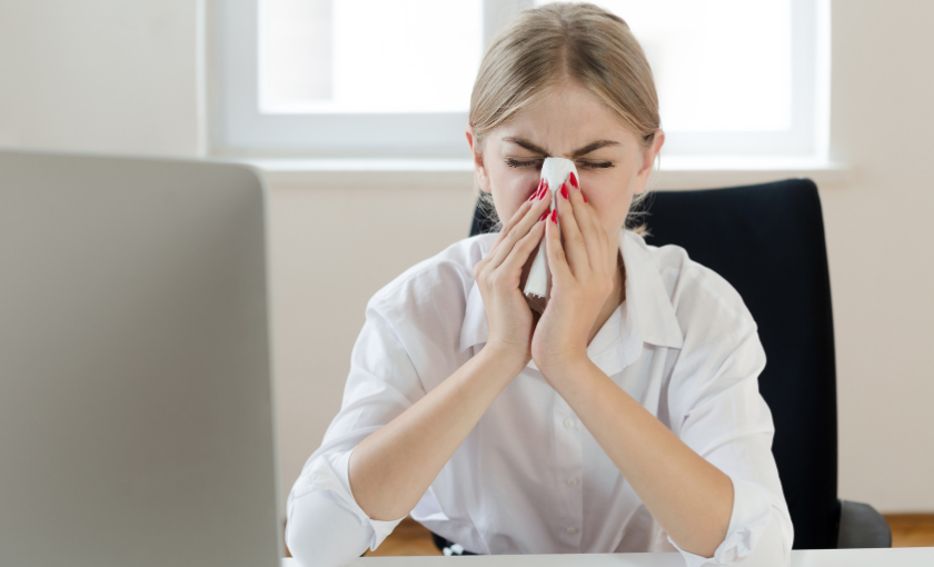 Erkältete Mitarbeiterin schnäuzt sich im Büro: Erkältungen sind im Winter der häufigste Grund für Krankmeldungen